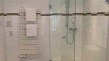 A modern bathroom with a glass-enclosed shower, a white towel rack, and a dark-tiled floor.