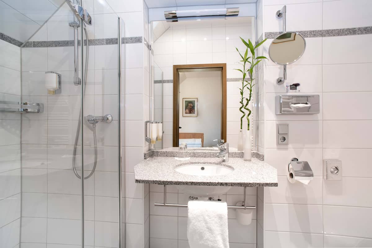 Une salle de bain moderne avec une douche à parois de verre, un lavabo sur un plan de travail en granit, un miroir et un porte-serviettes.
