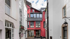 A narrow street with a red building featuring a glass entrance and outdoor seating. - UNO Hotel Posthof Saarlouis by ANS (Saarlouis)