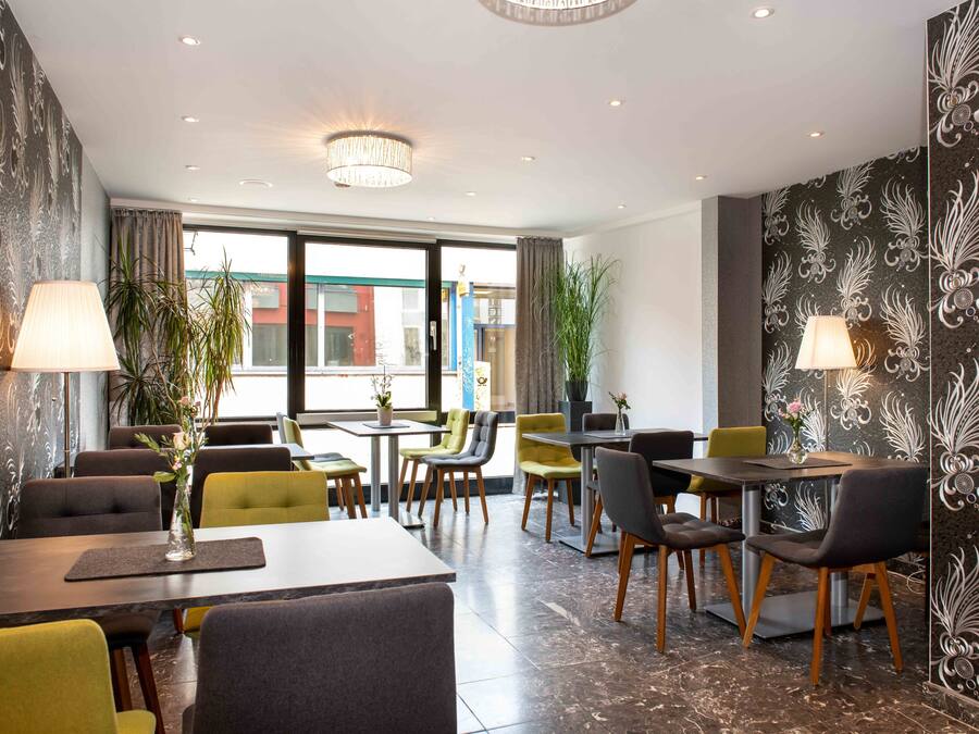 A modern dining area with tables and chairs, potted plants, and decorative wall panels.