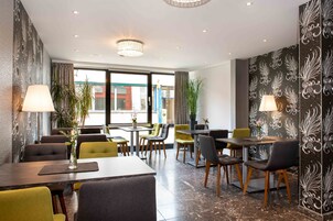 A modern dining area with tables and chairs, potted plants, and decorative wall panels.