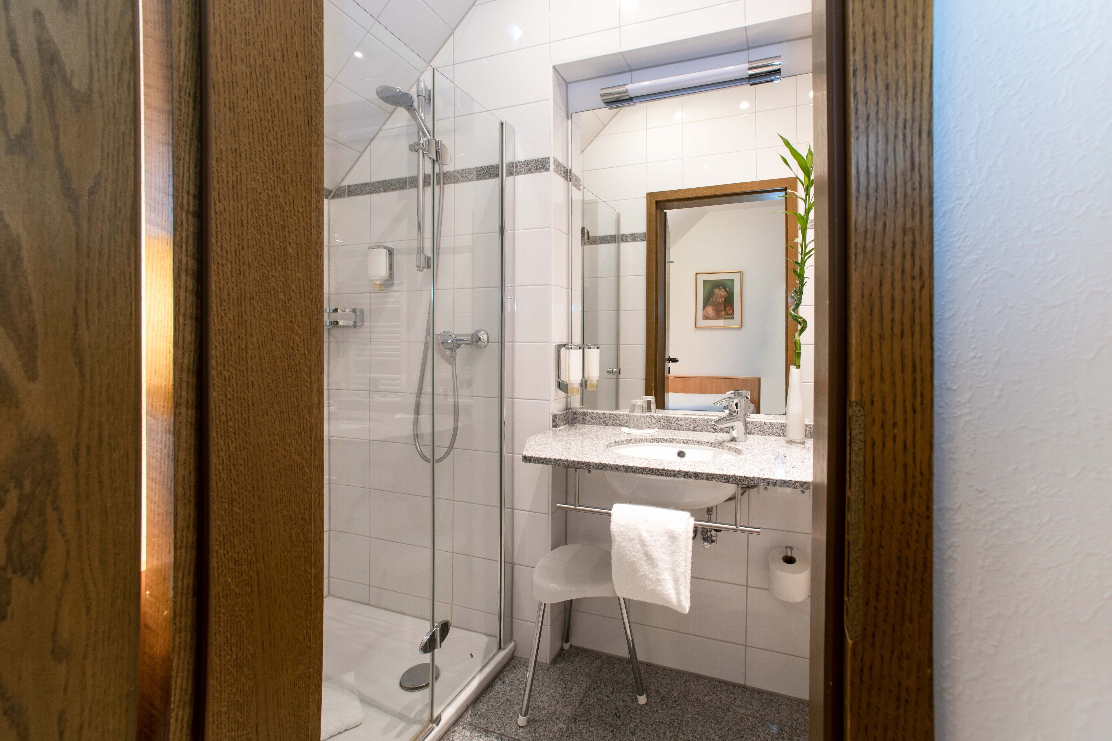 A modern bathroom with a glass-enclosed shower, a granite countertop sink, and a white towel hanging on a rack.