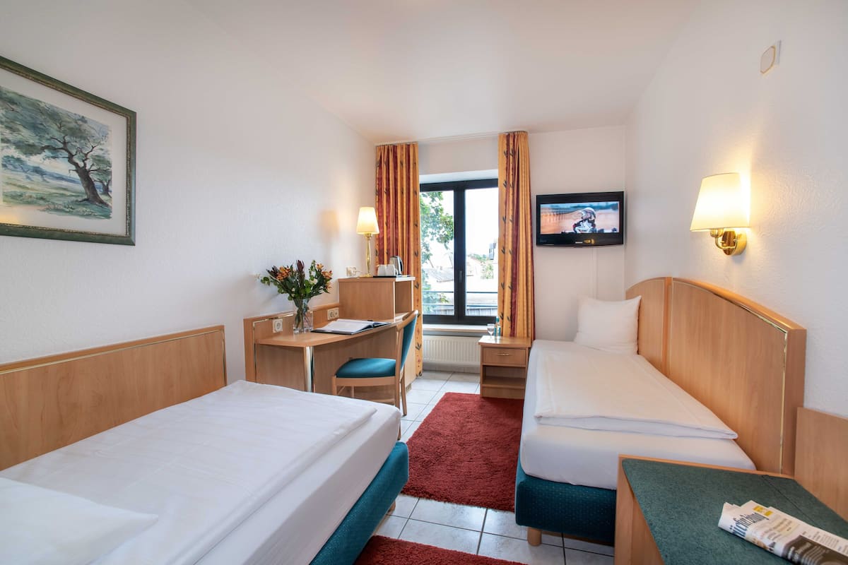 Une chambre d’hôtel avec deux lits, un bureau, une chaise, une télévision et une fenêtre avec des rideaux.