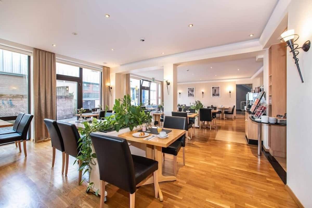 Un vaste espace dédié à la salle à manger, doté d’un plancher en bois, de chaises noires et d’une table centrale agrémentée d’une plante.