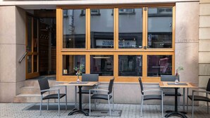 An outdoor seating area with tables and chairs, a wooden-framed window, and a door leading to an interior space. - UNO Hotel Posthof Saarlouis by ANS (Saarlouis)
