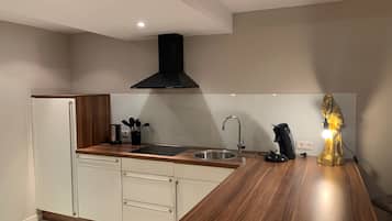 A modern kitchen with a wooden countertop, stainless steel sink, and a black range hood.