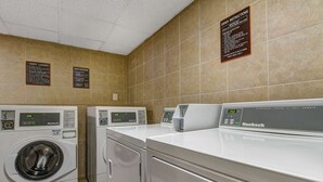 Une buanderie d’hôtel équipée de plusieurs machines à laver et de plusieurs séchoirs, dont une machine à laver à chargement frontal et une machine à laver à chargement par le haut.