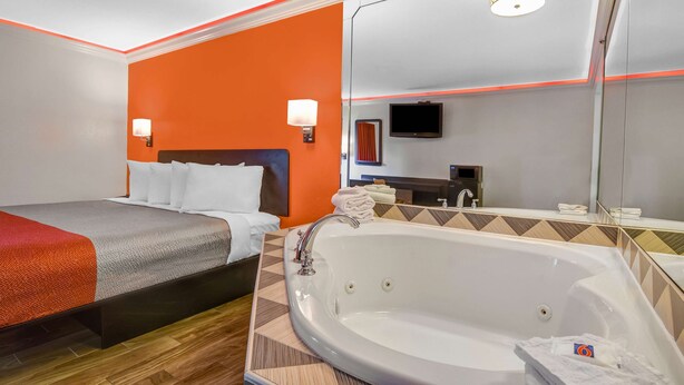Une chambre d’hôtel avec un lit, une grande baignoire, un miroir et un téléviseur.