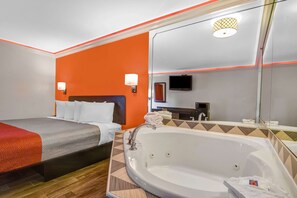 A hotel room with a bed, a large bathtub, a mirror, and a television. - Motel 6 Norcross, GA (Peachtree Corners)
