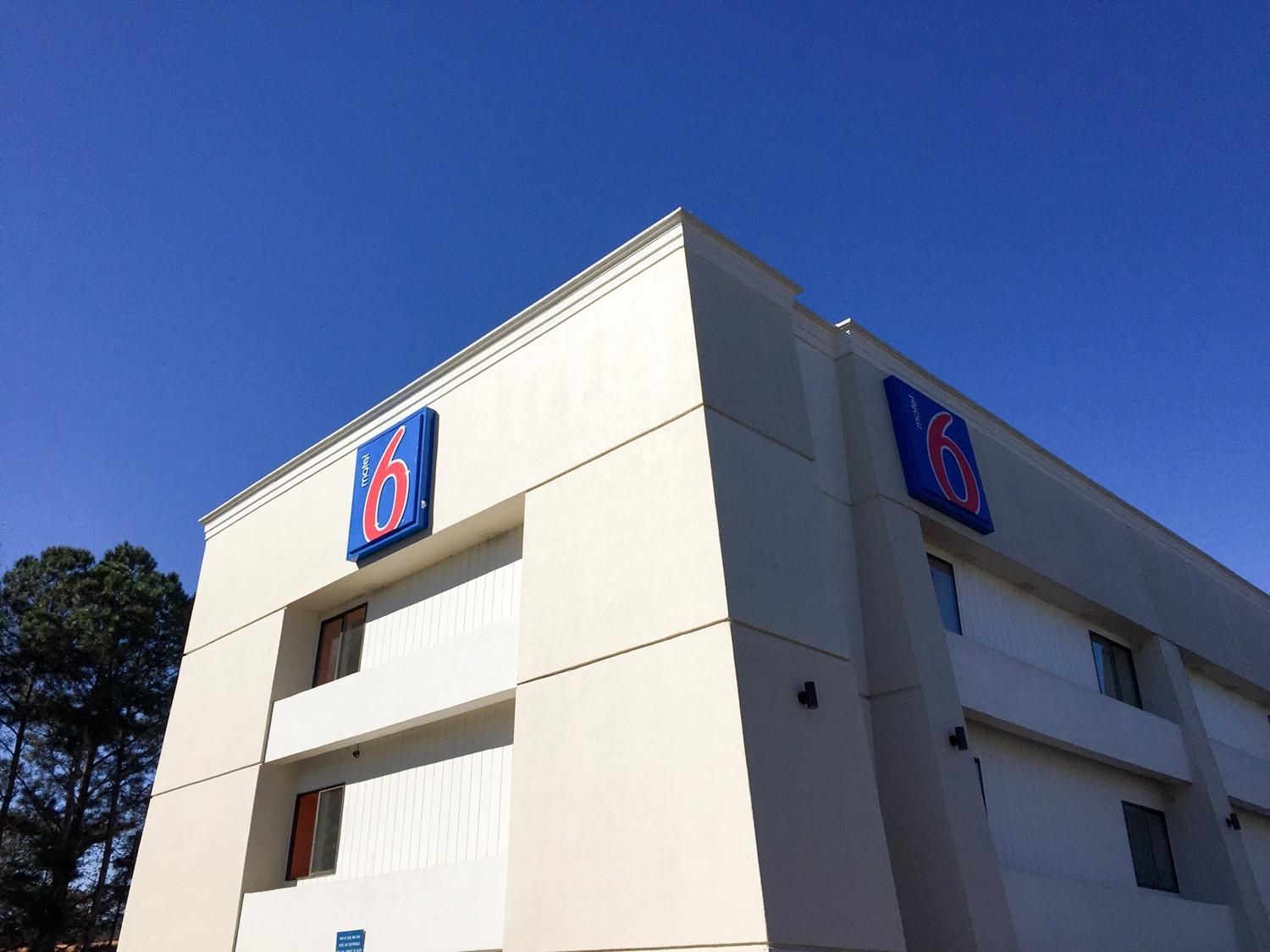Un bâtiment d’hôtel avec un grand logo en forme de « 6 » sur la façade, de nombreuses fenêtres et un toit plat.
