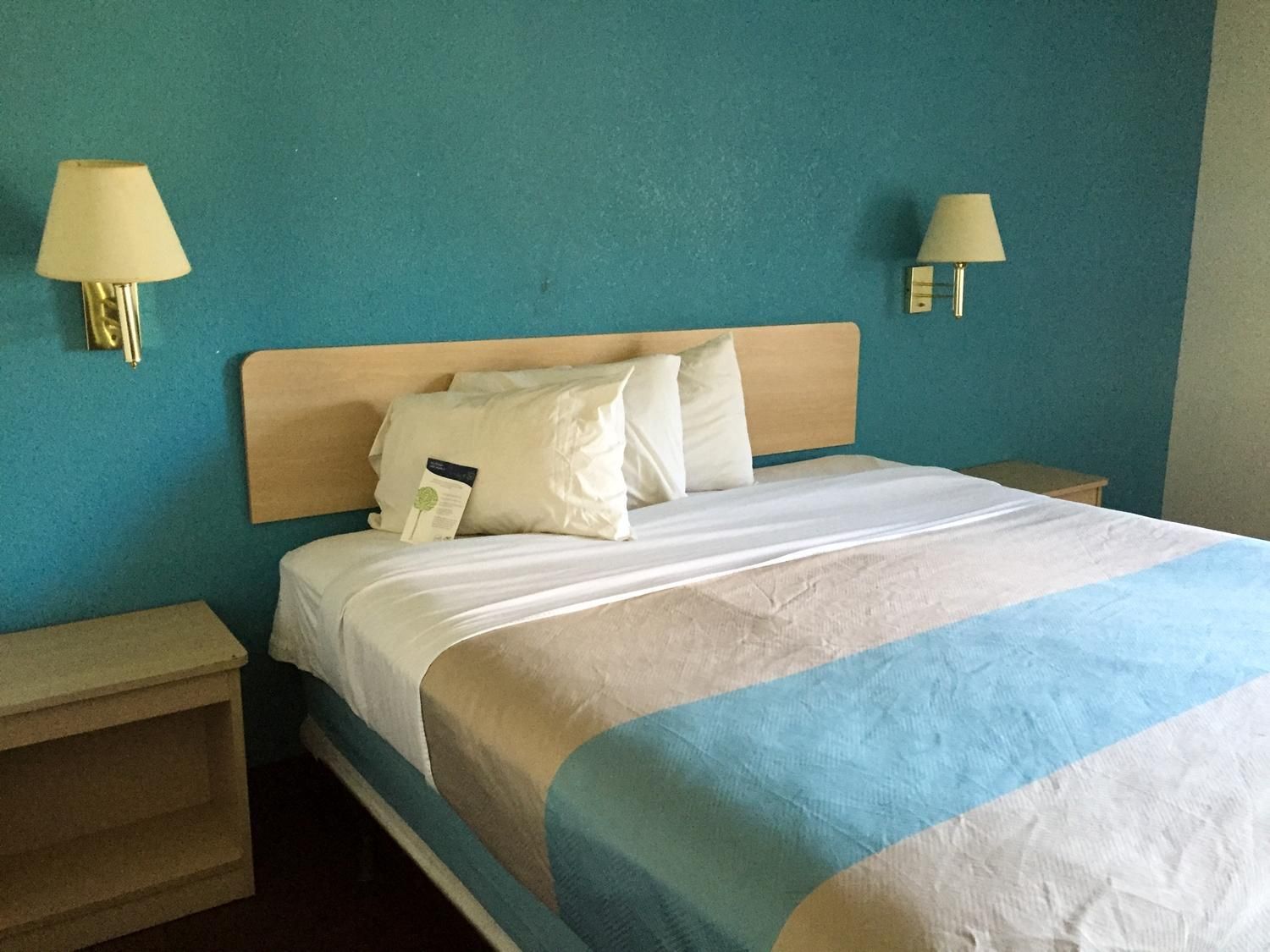 Una habitación de hotel con una cama, dos mesitas de noche y dos lámparas de pared.