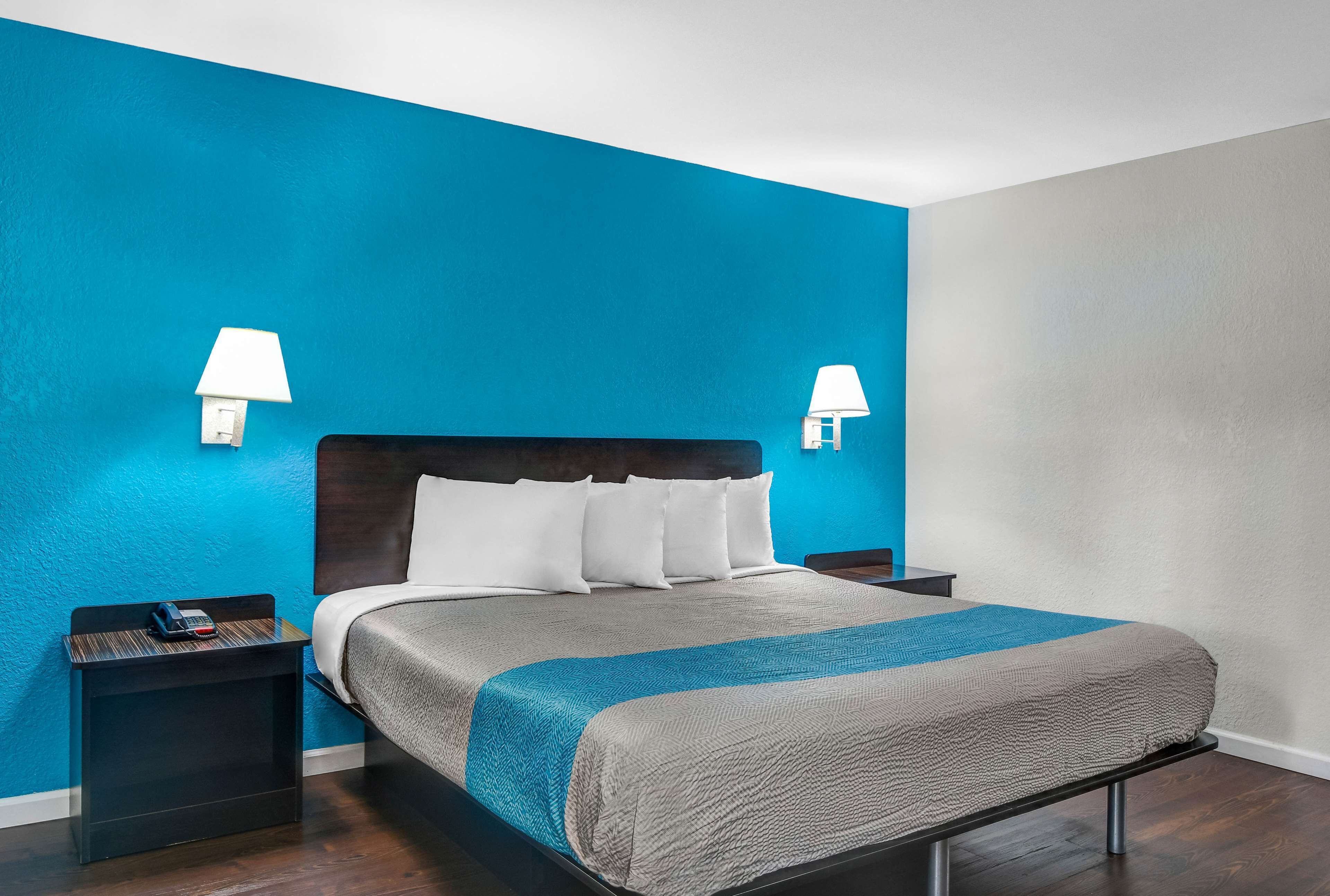 A hotel room with a bed, two bedside tables, a nightstand, and two wall-mounted lamps.