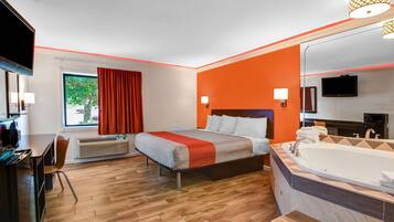 Une chambre d’hôtel comprenant un lit, une grande fenêtre avec des rideaux, un bureau, une chaise, une télévision et une salle de bain avec une baignoire et un miroir.