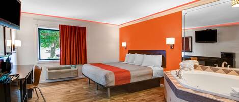 A hotel room with a bed, a large window with curtains, a desk, a chair, a TV, a bathroom with a bathtub, and a mirror.