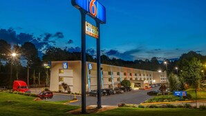 Un motel avec un grand panneau indiquant le chiffre « 6 », un parking et une entrée bien éclairée.