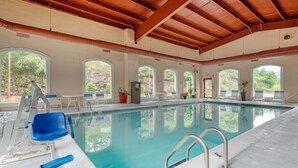 Una piscina interior con agua azul cristalina, rodeada de paredes blancas y amplias ventanas arqueadas.
