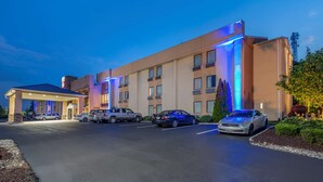 Un hotel con estacionamiento techado, varios coches aparcados y una fachada bien iluminada.