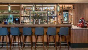 Zona de bar con taburetes, estantes llenos de botellas de licor y lámparas colgantes.