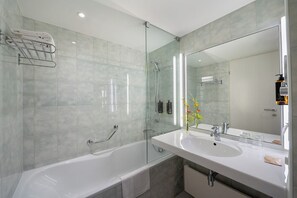 Une salle de bain moderne avec une baignoire, deux lavabos, une douche à parois de verre et un grand miroir.