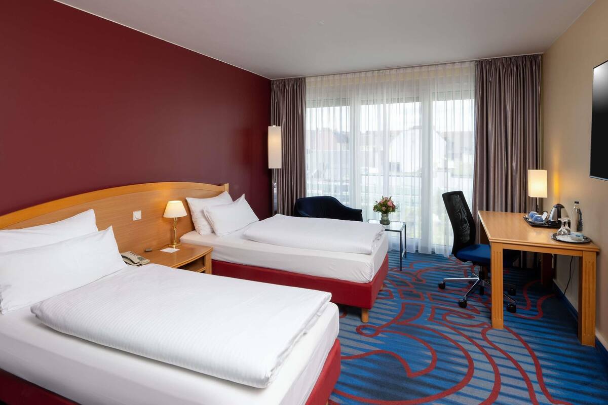 Een hotelkamer met twee bedden, een bureau, een stoel, een televisie en een raam met gordijnen.