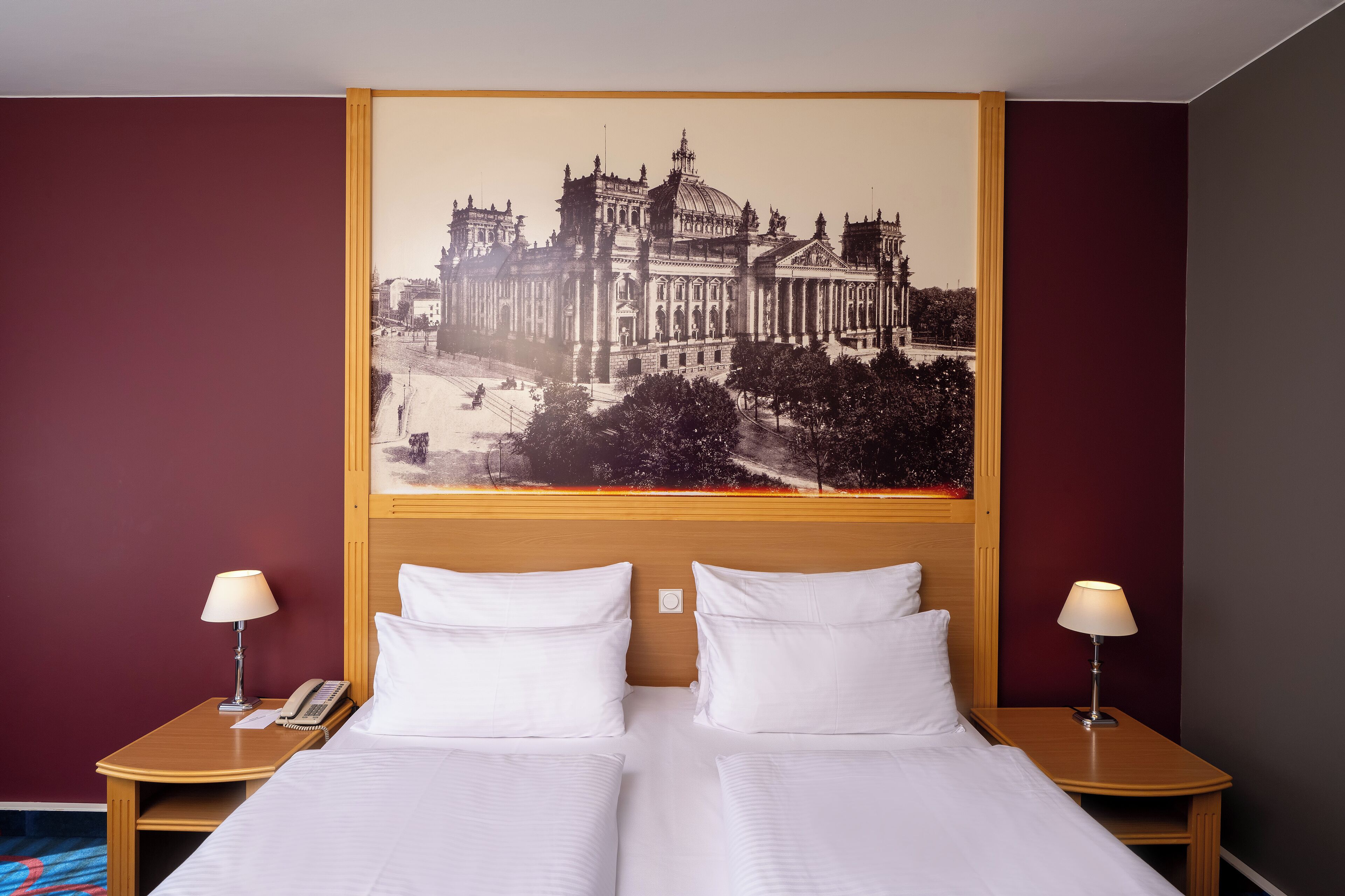 A hotel room with a large bed, two bedside tables, and a wall-mounted picture of a historic building.