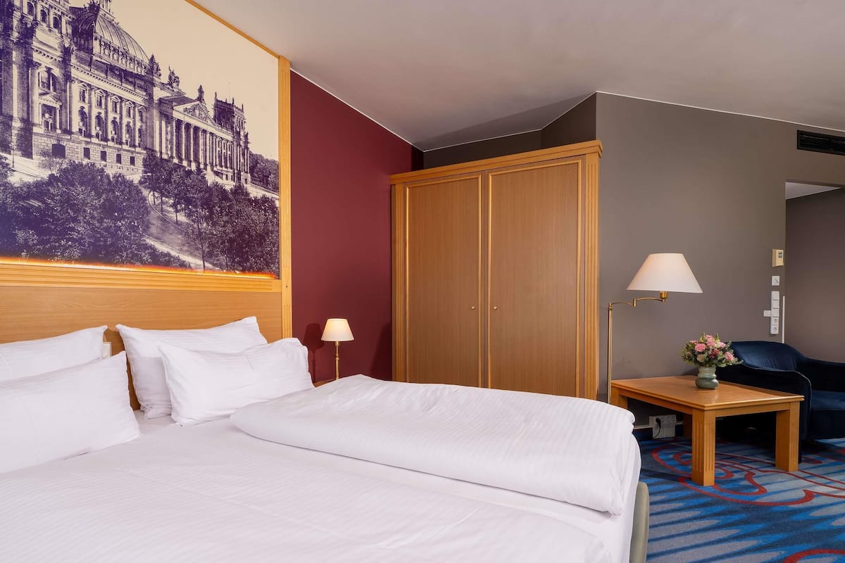 Een hotelkamer met een groot bed, een houten garderobe, een bureau met lamp en een stoel.