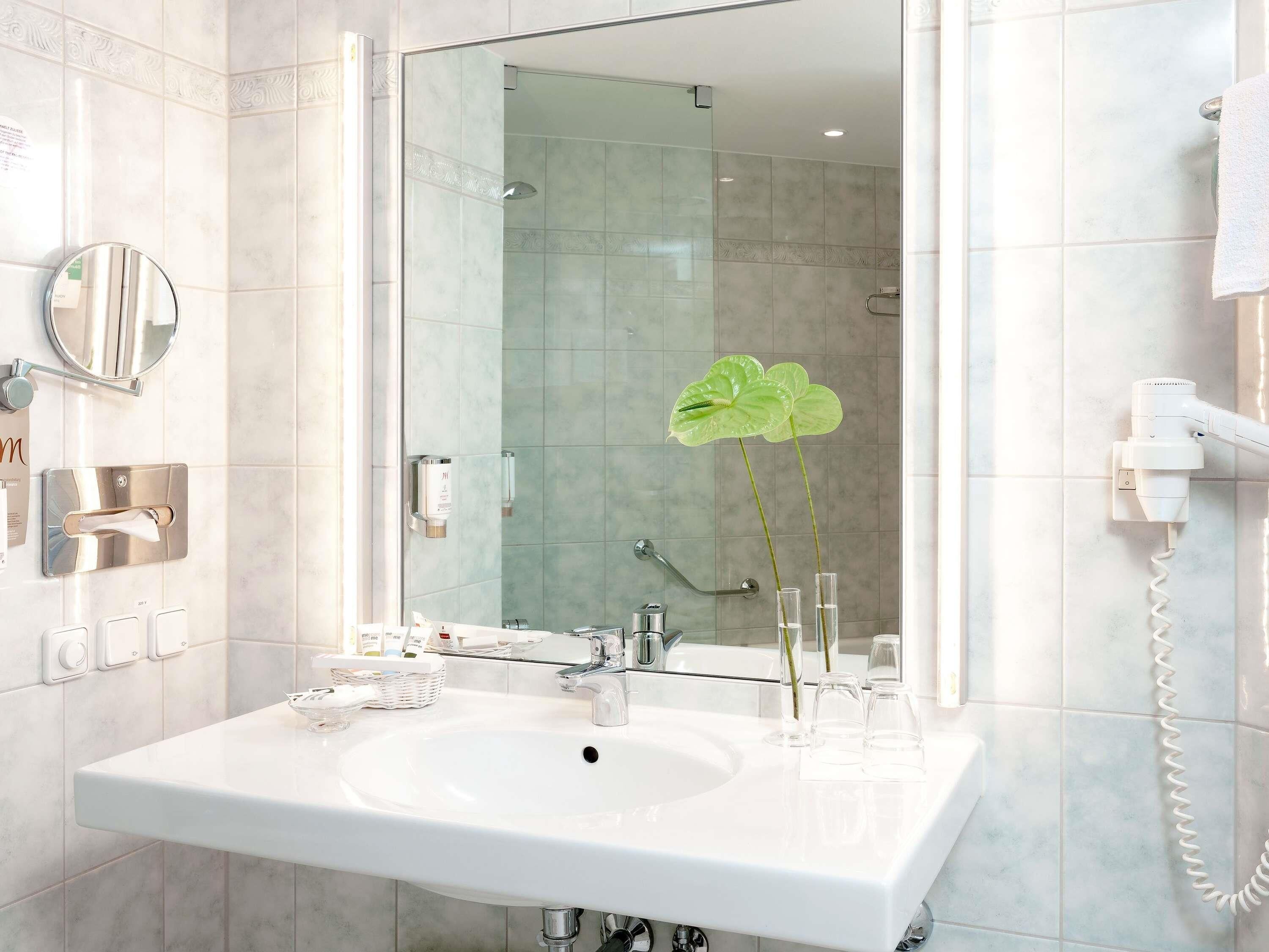 Een badkamer met een wit wastafelmeubel, een spiegel, een douchecabine van glas en een handdoekrek.
