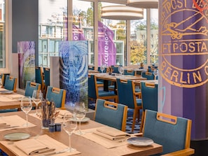 Un restaurant avec des tables dressées, des chaises et une vue sur l’extérieur.