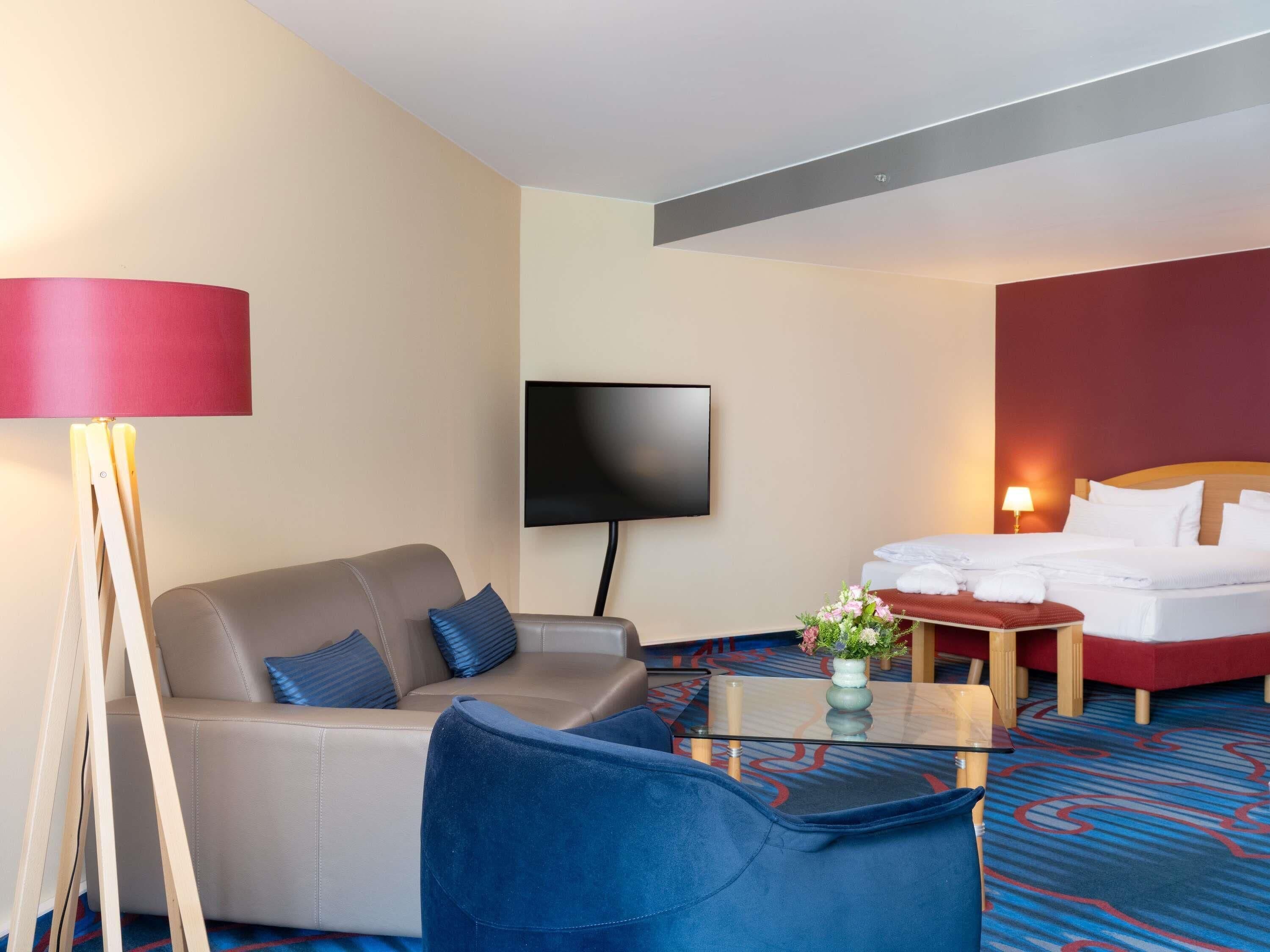 Una habitación de hotel con sofá, sillón, cama, televisión y mesa de centro.