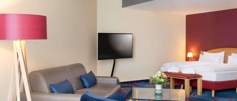 Una habitación de hotel con sofá, sillón, cama, televisión y mesa de centro.
