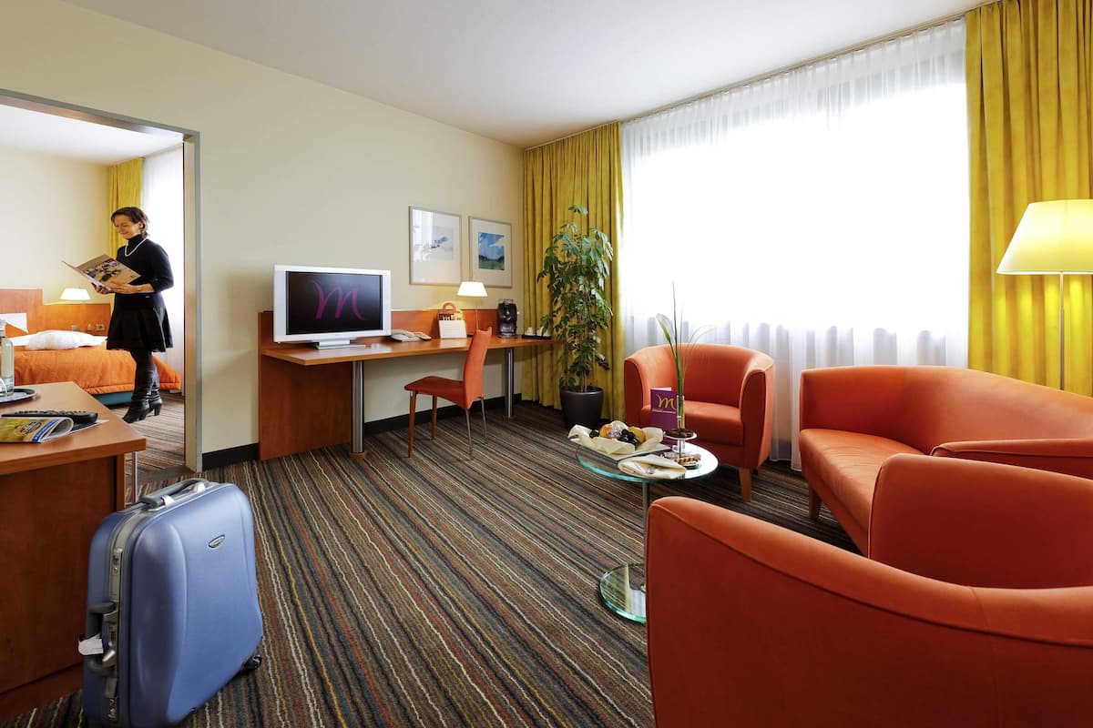 Habitación de hotel con cama, escritorio, televisión, sillón y maleta.