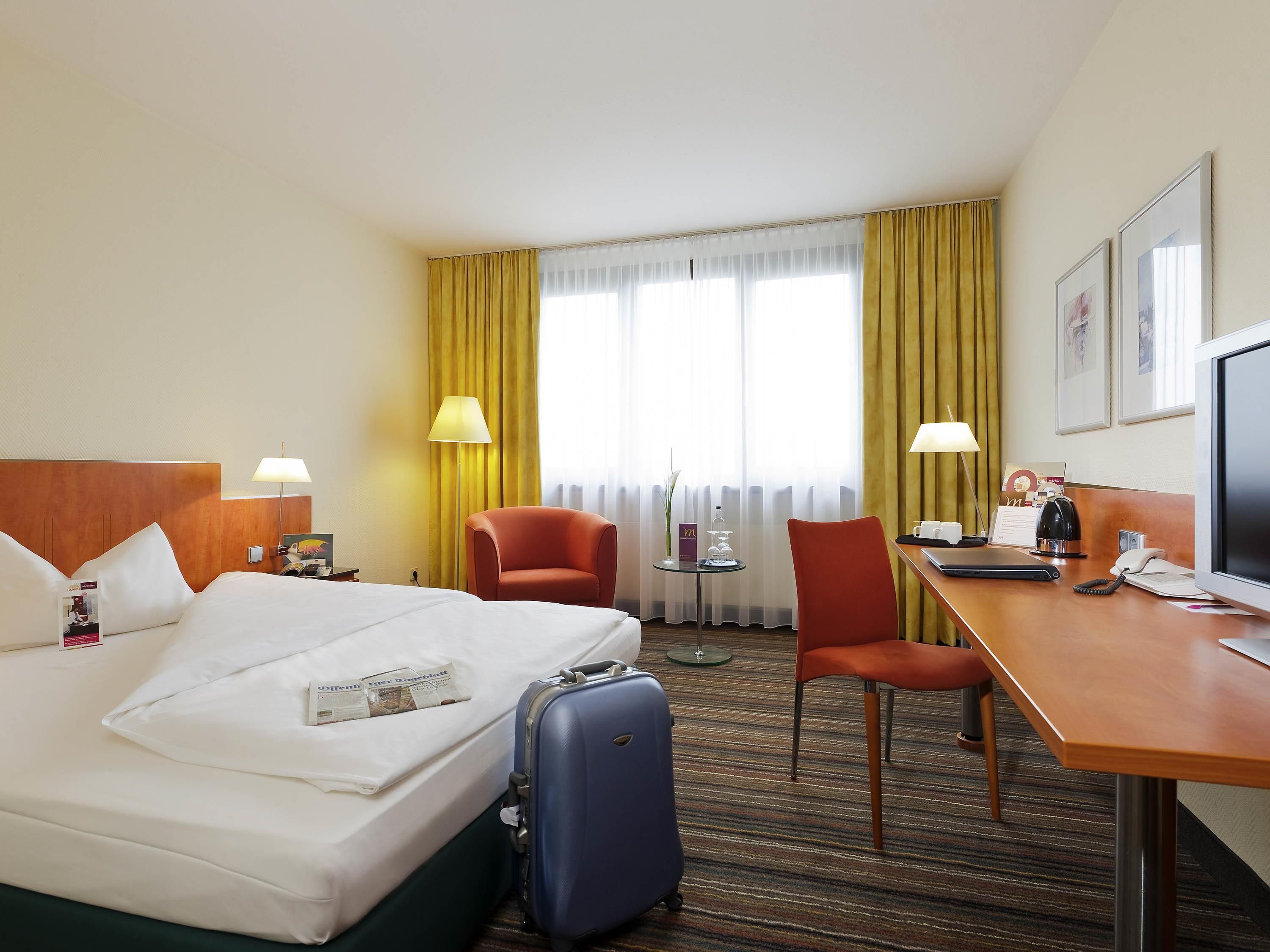 Ein Hotelzimmer mit Bett, Schreibtisch, Stuhl, Schreibtischlampe, Fernseher und einem Fenster mit Vorhängen.