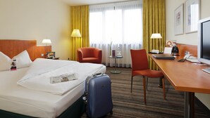 A hotel room with a bed, a desk, a chair, a desk lamp, a television, and a window with curtains. - Mercure Hotel Offenburg am Messeplatz (Offenburg)