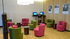 Un espace d’attente moderne avec des chaises vertes et roses, un plancher en bois et deux ordinateurs placés sur une étagère.