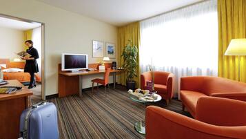 Ein Hotelzimmer mit Bett, Schreibtisch, Fernseher, Sessel und Koffer.