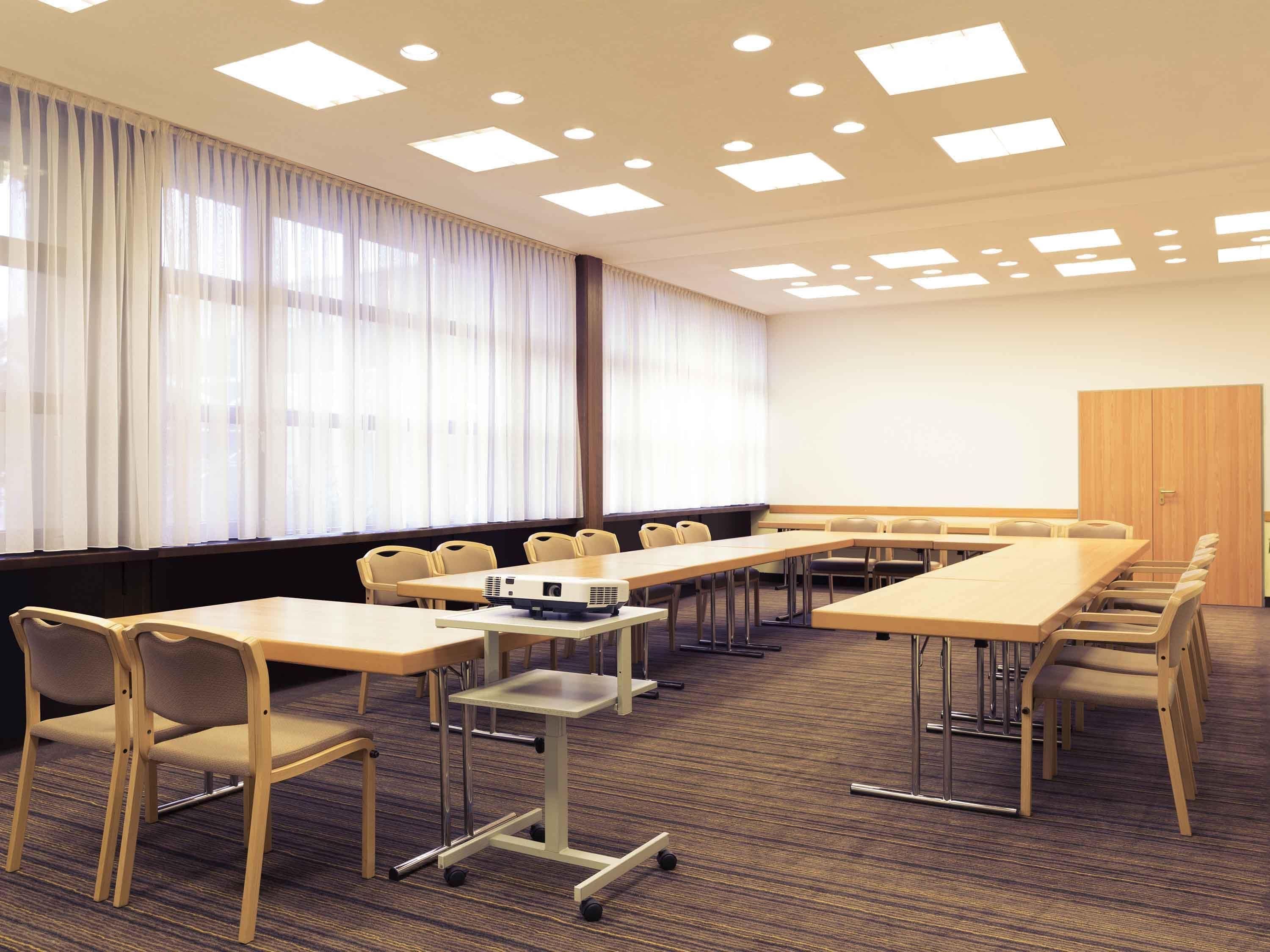 A conference room with a long table, chairs, a projector, and a large window with curtains.