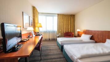 Une chambre d’hôtel équipée d’un bureau, de deux lits, d’une télévision et d’une fenêtre avec des rideaux.
