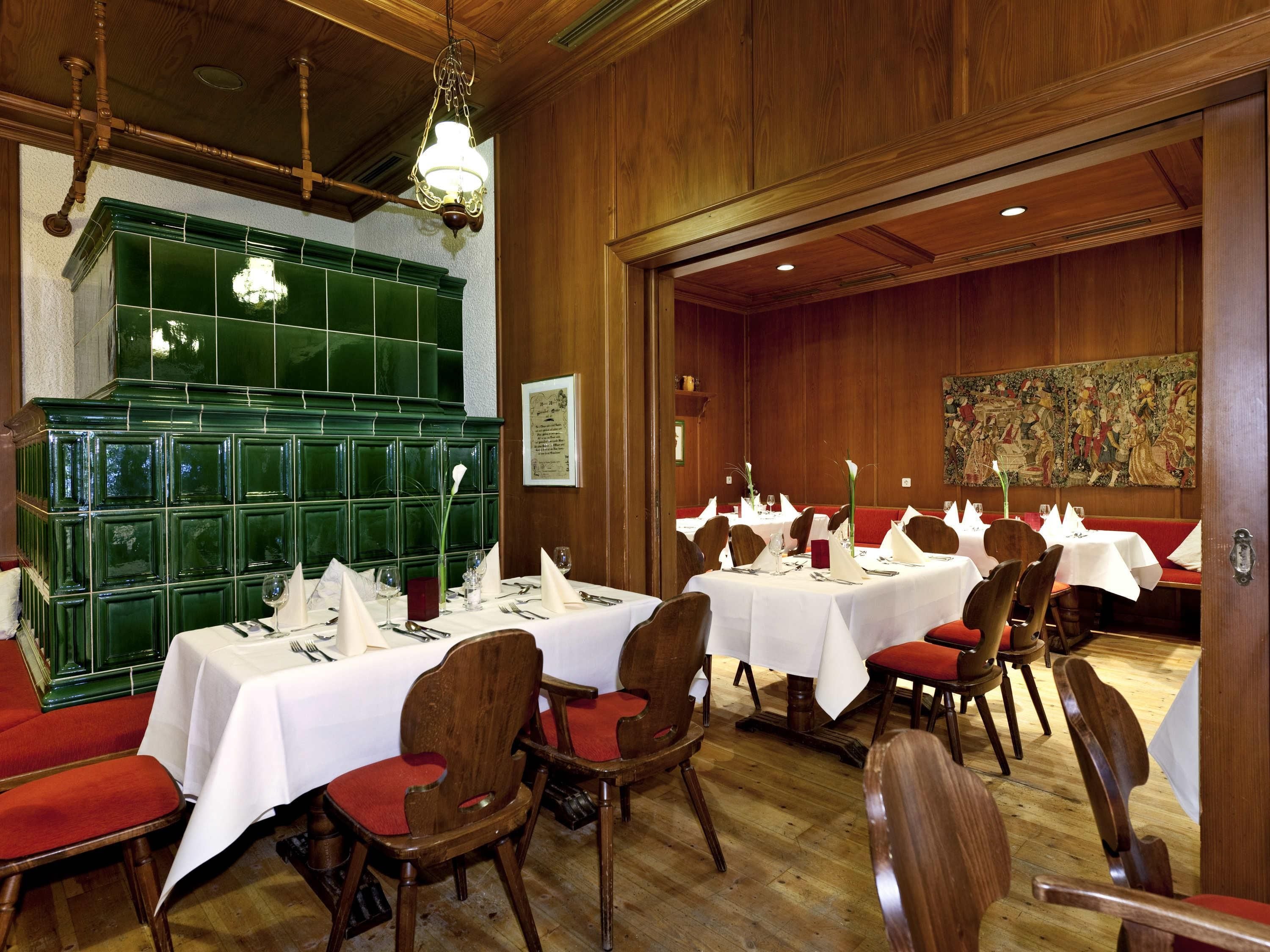 A restaurant with multiple tables set for dining, wooden paneling on the walls, and a green tiled backsplash.