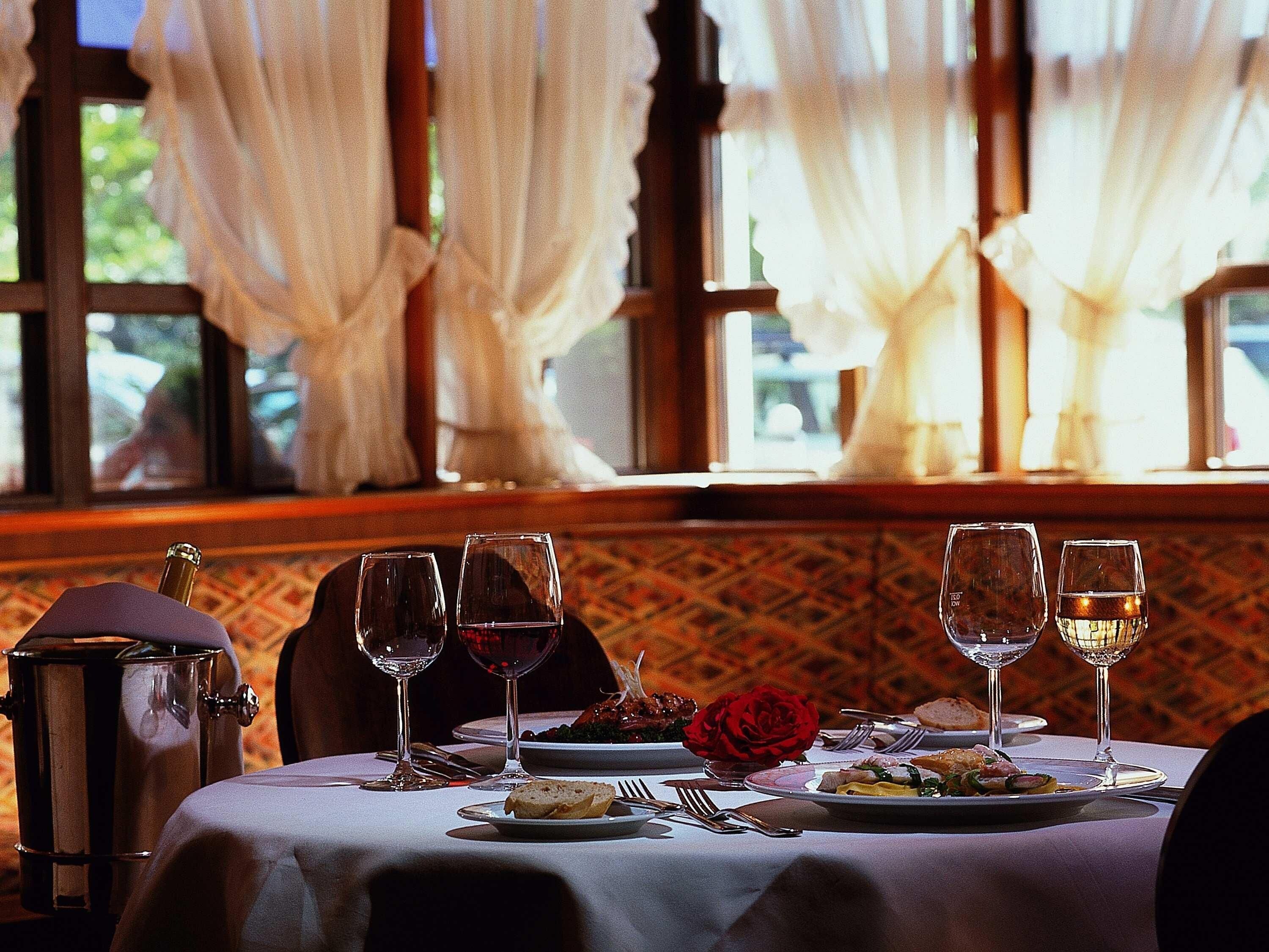 Una mesa de comedor dispuesta con platos, vasos y cubiertos, con un centro de rosas y un candelabro.