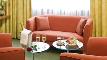 Una habitación con un sofá rojo, una mesa de vidrio con una bandeja de frutas, dos copas de champán y un jarrón con una rosa.