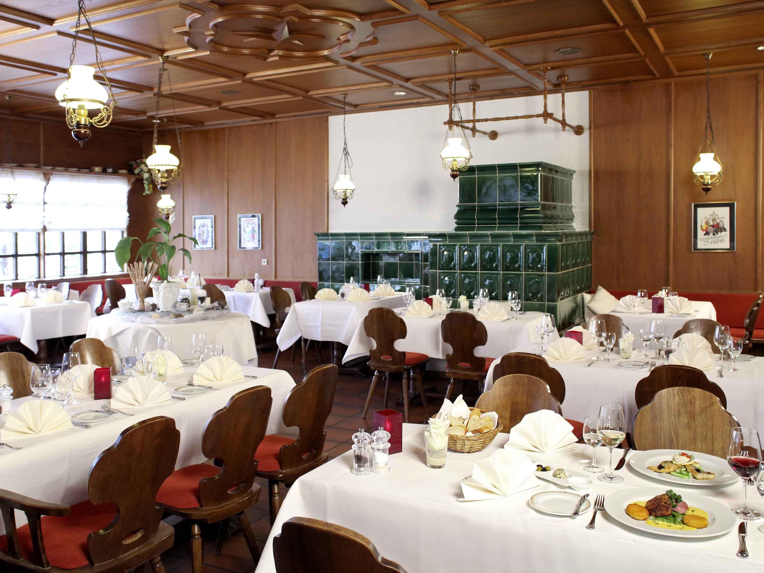 A dining area with multiple tables set for meals, wooden chairs, and hanging chandeliers.
