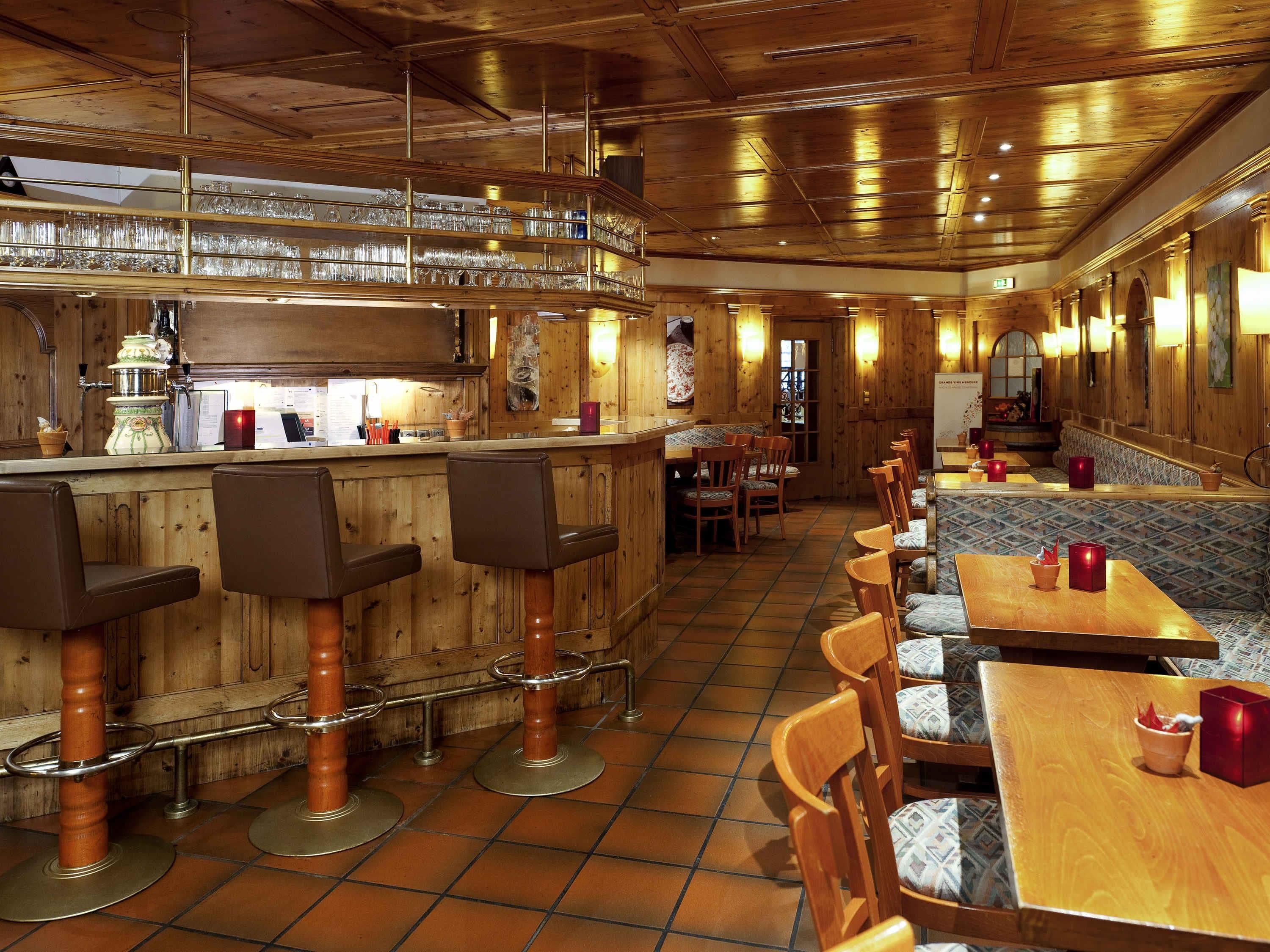 Un restaurante con interiores de madera, taburetes, mesas y una zona de bar con vasos.