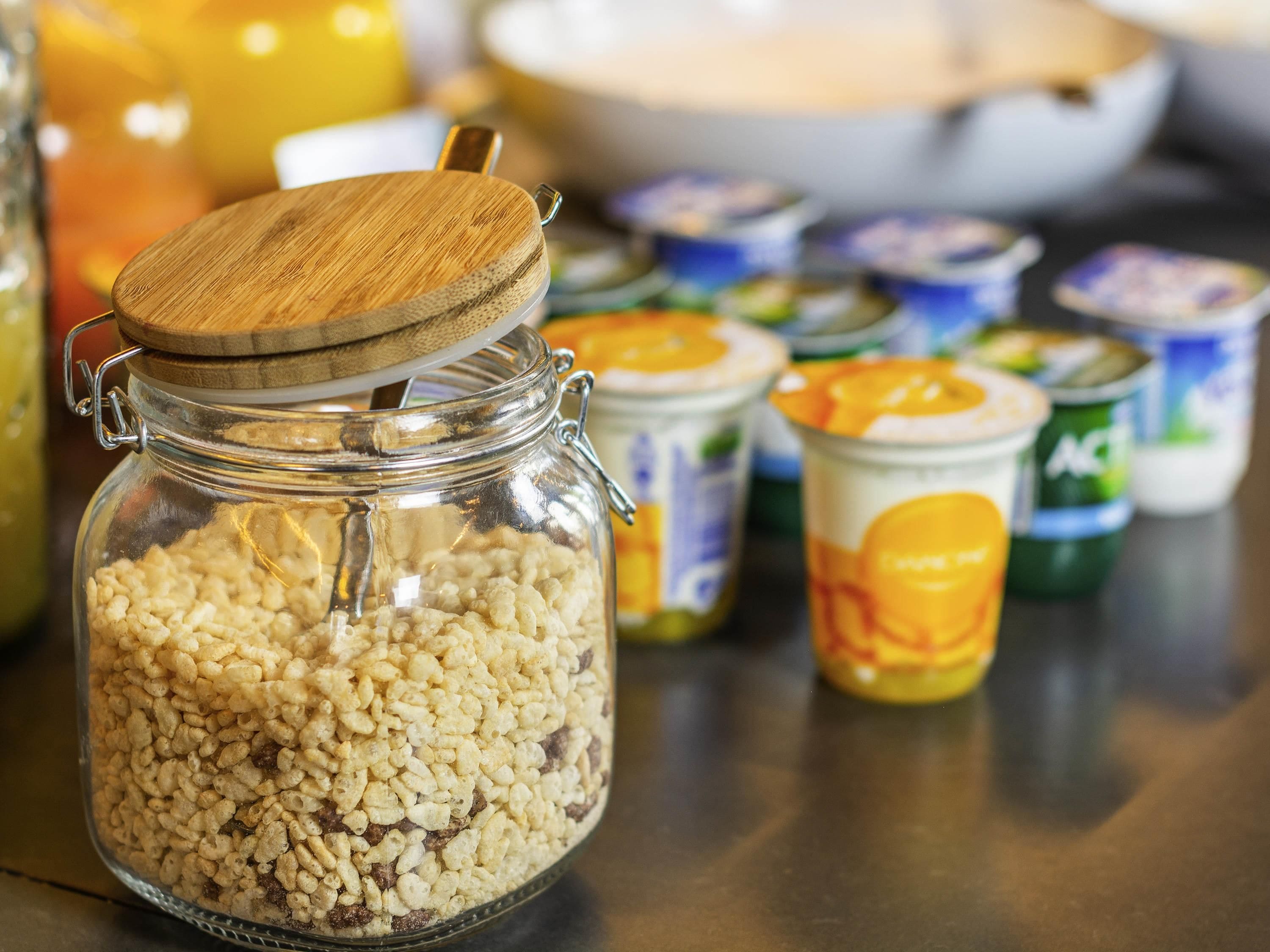 A glass jar filled with cereal flakes, surrounded by various food containers.