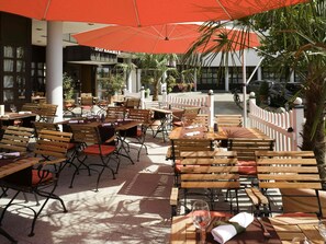 Un espace de restauration en plein air avec des tables et des chaises en bois, des parasols et une clôture blanche.