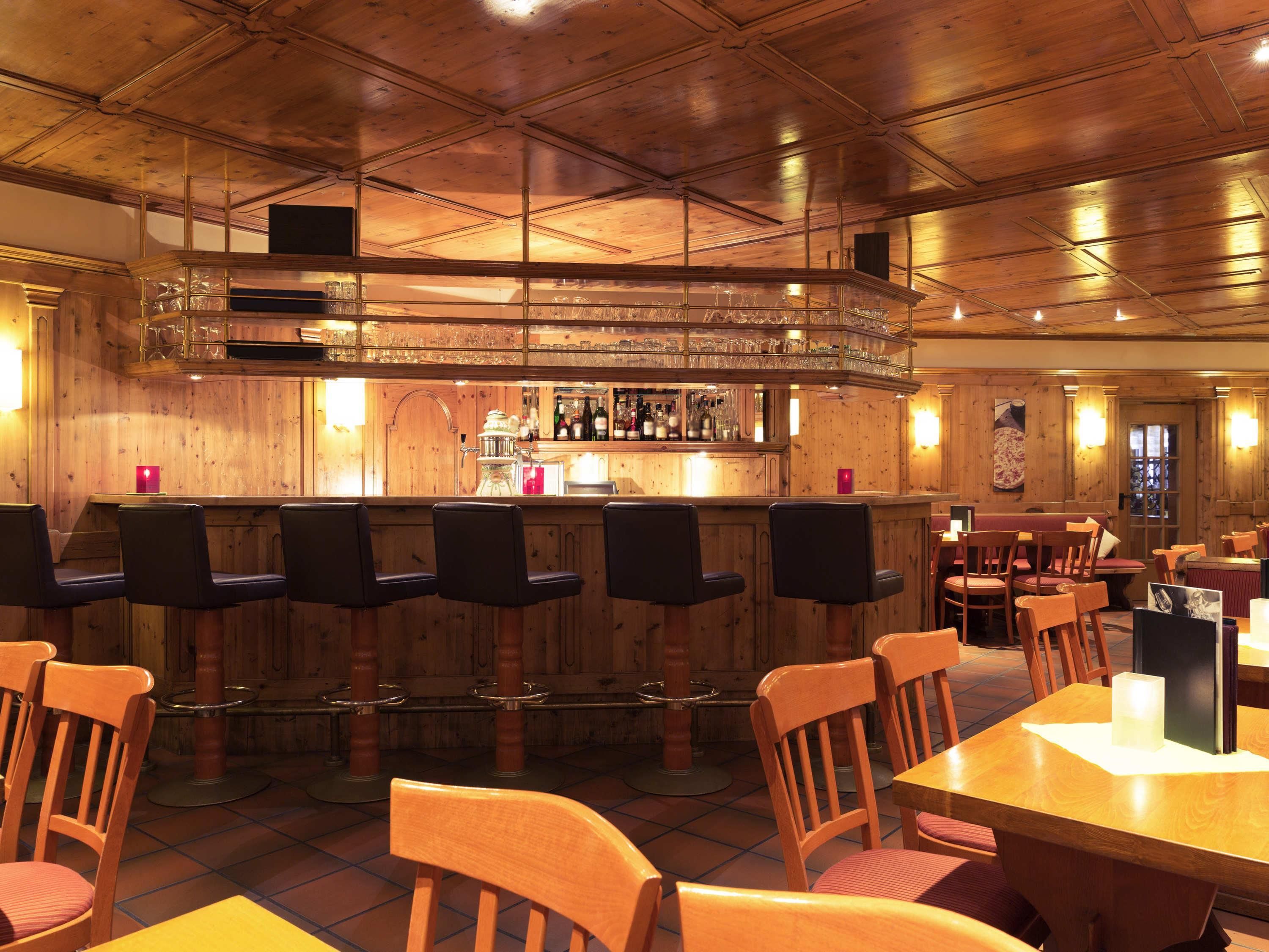Zona de bar con taburetes de madera y una barra con botellas y vasos.