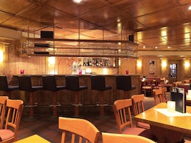 A bar area with wooden bar stools and a counter with bottles and glasses.