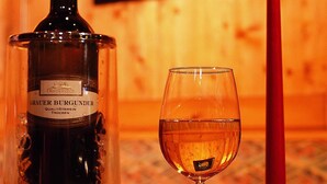 Une bouteille de vin Bräuer Burghof, un verre de vin et une bougie rouge dans une pièce éclairée d’une lumière chaleureuse.