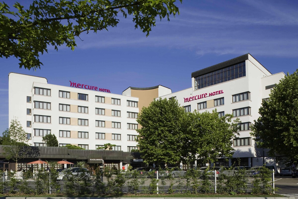 A Mercure Hotel with a modern facade, multiple floors, and a parking area in front.