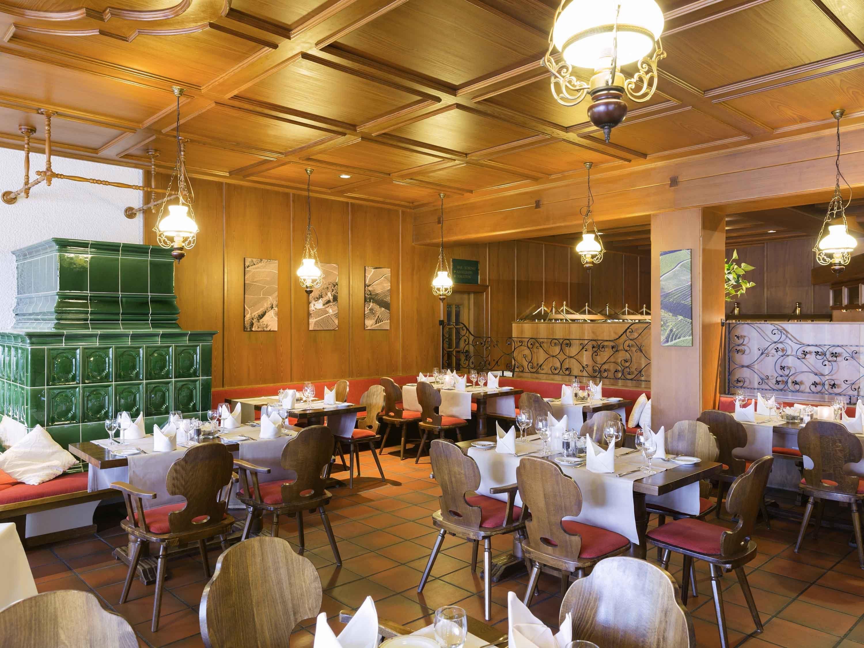 A restaurant with wooden paneling, multiple dining tables set with white tablecloths and red cushioned chairs.