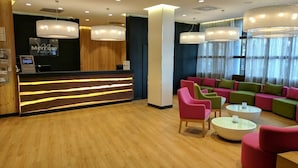Un hall d’hôtel doté d’un comptoir d’accueil, d’un éclairage moderne et d’espaces de détente aux couleurs vives.